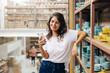 © (JLco) Julia Amaral - Happy ceramic store owner reading a text message in her shop