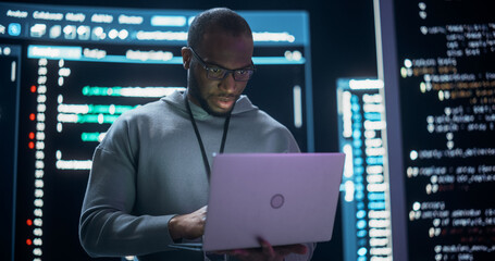Leinwandbilder - Portrait of Professional Programmer Developing a Big Data Interface Software Project.Young Black Man Working on Laptop Computer, Looking at Big Digital Screen Displaying Back-end Code Lines