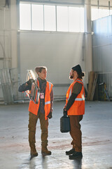 Poster - Two young engineers in protective reflective jackets discussing something at working meeting while one of them listening to colleague