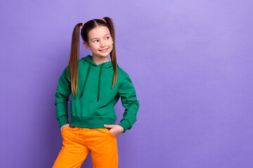 Portrait of funny cute sweet little pupil girl look empty space wear sports clothes sweatshirt pants isolated purple color background