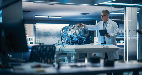 Fototapete - Jet Engine Specialist Working on a Project with Futuristic Turbine Motor, Standing with Tablet Computer in Scientific Technology Lab. Middle Aged Science Professor Developing a Futuristic Engine