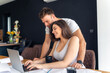 © DusanJelicic - The expectant mother works from home before going on maternity leave, her husband standing behind her, an untidy table and a laptop