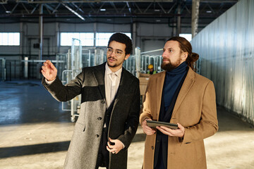 Leinwandbilder - Young confident owner of industrial factory showing new equipment to male colleague in formalwear holding tablet and looking forwards