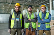 © pressmaster - Group of happy young intercultural workers of warehouse or factory in safety helmets and fluorescent jackets standing in front of camera