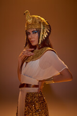 Elegant woman in egyptian look and headdress looking at camera on brown background