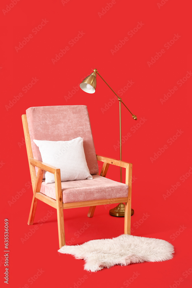Soft armchair, rug and lamp on red background