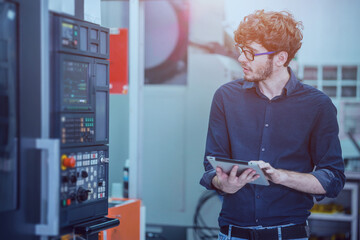 Professional young engineer factory worker programming CNC milling machine with a tablet computer.