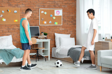 Wall Mural - Sporty male students playing with soccer ball in dorm room