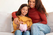 © Prostock-studio - Happy Mom And Daughter Putting Coin In Piggybank At Home