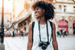 © Dusko - Young black female tourist enjoys walking through the streets of a beautiful European city. She is happy and using her photo camera to take fantastic architecture photographs. Bright sunny day.