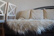 Gray sofa with boucle upholstery fabric and white decorative fluted cushions. White rug or bedspread made of faux fur with a long pile. Living room interior. Wooden painted chairs.