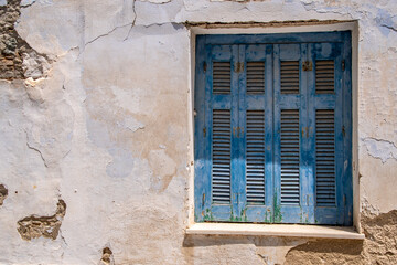 Old blue shutters - charming Rustic decay in traditional European village showing old stones, worn wood, awaiting restoration in the beautiful village Greek Island - Tinos Island.