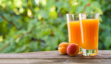 Glasses Of Apricot Juice On Wooden Table On Green Background. Freshly Picked Apricots In The Garden On An Old Wooden Table. Fresh Apricots On A Wooden Table Over Blurred Green Background