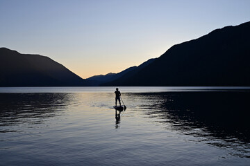 Wall Mural - Male paddleboarder in silhouette at sunset on Lake Crescent in Olympic National Park, Washington on calm clear summer afternoon.