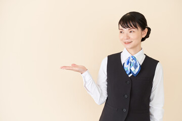 手で案内するベストにリボンタイの制服を着た、受付業務、事務業務の女性