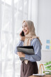 © David - Young business Asian Business muslim woman in purple hijab using tablet and phone, standing near the window in workplace business finance concept.
