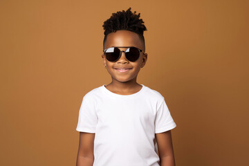 Wall Mural - design mockup: black little boy with sunglasses and blank white t-shirt on a brown background