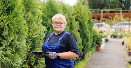 Thuja tree farm, Senior gardener woman using tablet computer for garden shop control inventory flowers and plants