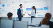 © Gorodenkoff - Male Data Scientist And Female Project Manager Discussing Reports And Graphs On Big Digital Screen In Modern Monitoring Office. Diverse Employees Working Behind Computers in Deep Learning Company.