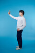 © makistock - full body young man doing selfie shot on mobile cell phone isolated on blue background