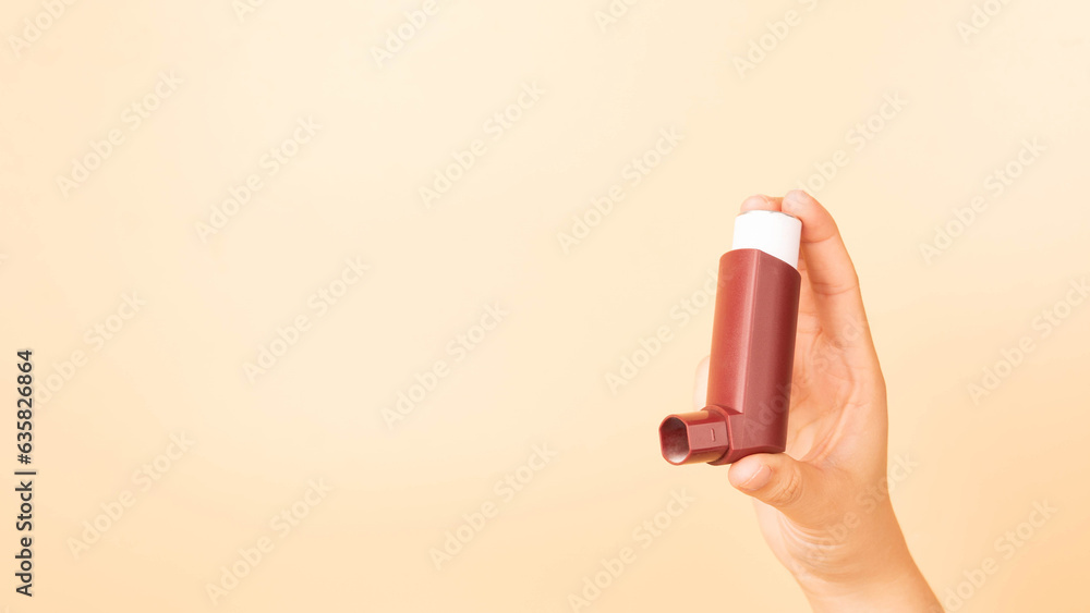 Hand holding brown asthma inhaler over orange background ...