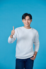 Wall Mural - Smiling young asian man wearing white jumper and jeans on blue background giving thumbs up