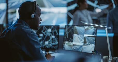 Aufkleber - African Specialist in a Dark High-Tech Monitoring Room, Concentrated on a Call and Computer Work. Black Technical Support Manager Using Headphones with Built-In Mic for Communication with Client