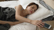 sleepy asian woman turning off ringing alarm on smartphone and roll over to continue sleep dream in early time. lazy lady in warm blanket does not wanna get up and hang up morning call on cellphone