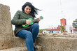 young latina woman of venezuelan ethnicity sitting outdoors learning to play ukulele