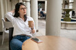 asian Japanese businesswoman having coffee and listening to podcast from earphones during break time from work in palo alto city California usa. she looks into space and feels a bit lazy