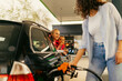 © DusanJelicic - A young mother fills up gas tank at a gas station while her daughters look out the window