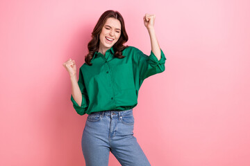 Photo of impressed excited woman dressed green shirt rising fists shouting empty space isolated pink color background