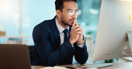 Thinking IT manager working on a desktop computer and laptop in a modern office. Information Technology software engineer analyzing data management system. Thoughtful analyst looking for a solution