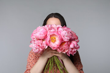 Poster - Young woman covering her face with bouquet of peonies on light grey background