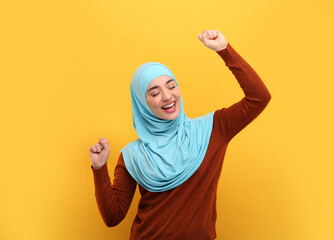 Wall Mural - Muslim woman in hijab dancing on orange background