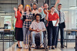 © .shock - A diverse group of young business people congregates within a modern startup's glass-enclosed office, featuring inclusivity with a person in a wheelchair, an African American young man , and a hijab