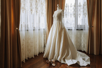 A luxurious lace wedding dress in an expensive interior of a hotel illuminated by natural light from a window on two sides