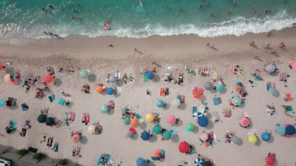 Sticker - Drone shot over sandy beach with people and colorful umbrellas and turquoise water