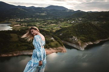 Poster - woman standing on top of a large cliff overlooking a lake