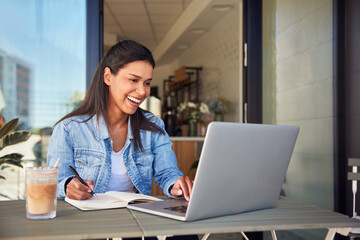 Young woman enjoying freelancer work from cafe using laptop and notepad