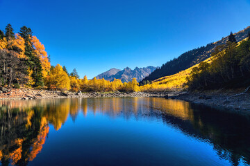 Beautiful landscape with mountain lake and high rocks with illuminated peaks reflection with green water, blue clean sky and yellow autumn sunrise.