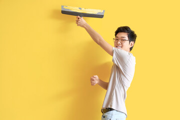 Young Asian man with putty knife on yellow background