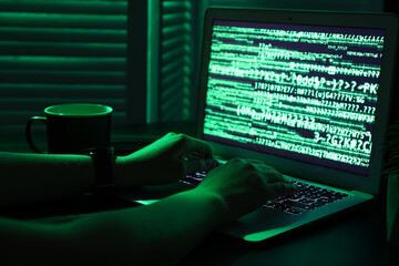 Female programmer typing on laptop keyboard at night in office, closeup