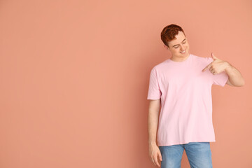 Wall Mural - Young man pointing at his t-shirt on beige background