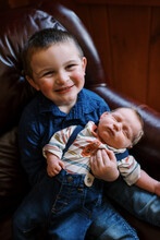 Little Boy Meeting His Newborn Baby Brother In Home On Couch