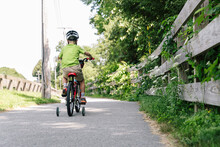 Young Boy Learns Riding Bike With Training Wheels And Helmet On Path