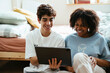 © BONNINSTUDIO/Stocksy - Smiling friends using tablet on bedroom