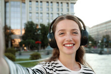 Portrait Of Smiling Woman In Headphones Taking Selfie On City Street