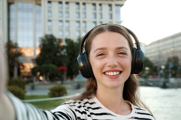 Portrait of smiling woman in headphones taking selfie on city street