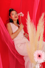 Elegant Asian Woman With Flower Leaning On Red Curtain